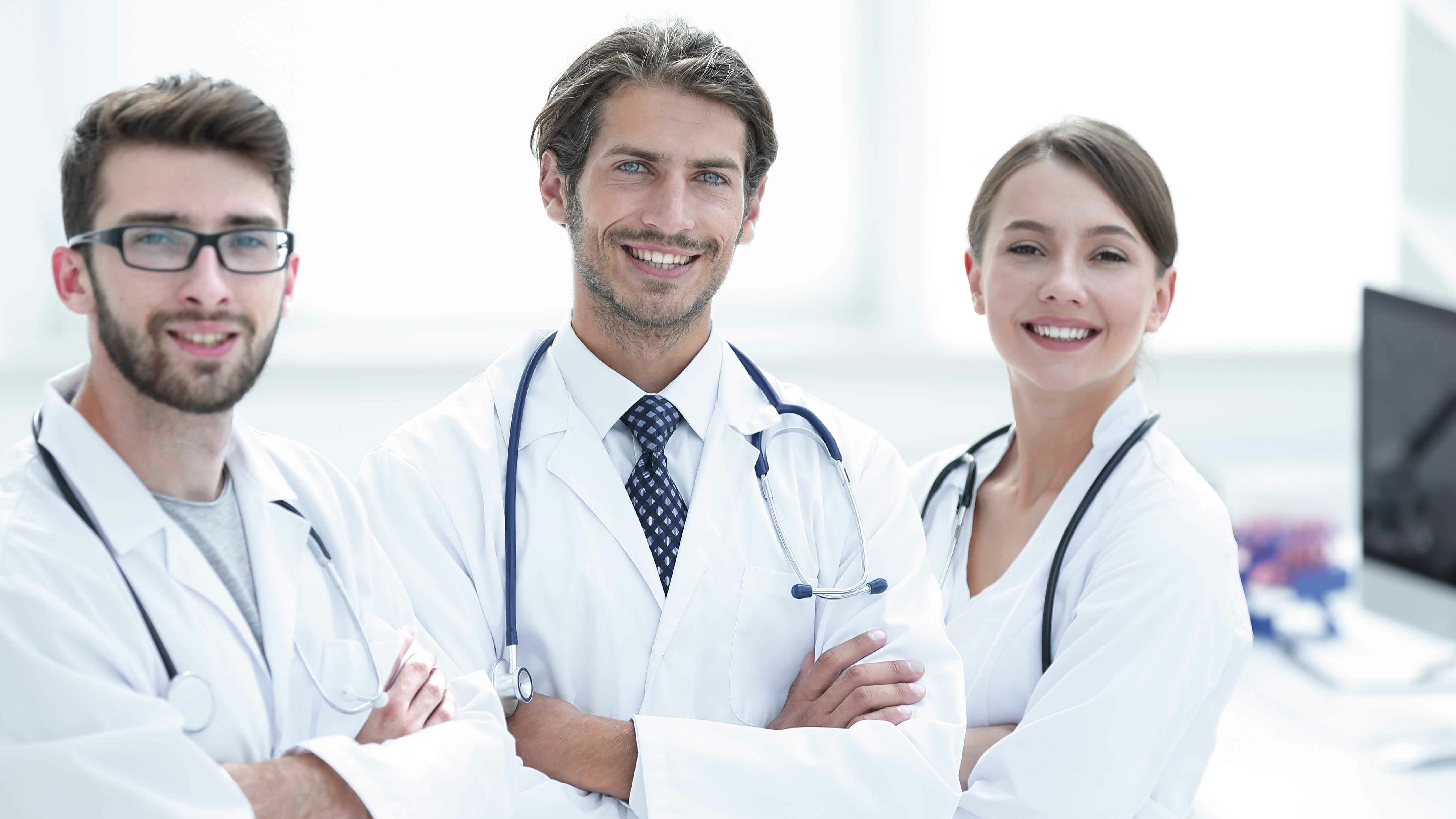 Drei freundliche Ärztinnen und Ärzte mit weißen Kitteln und Stethoskop