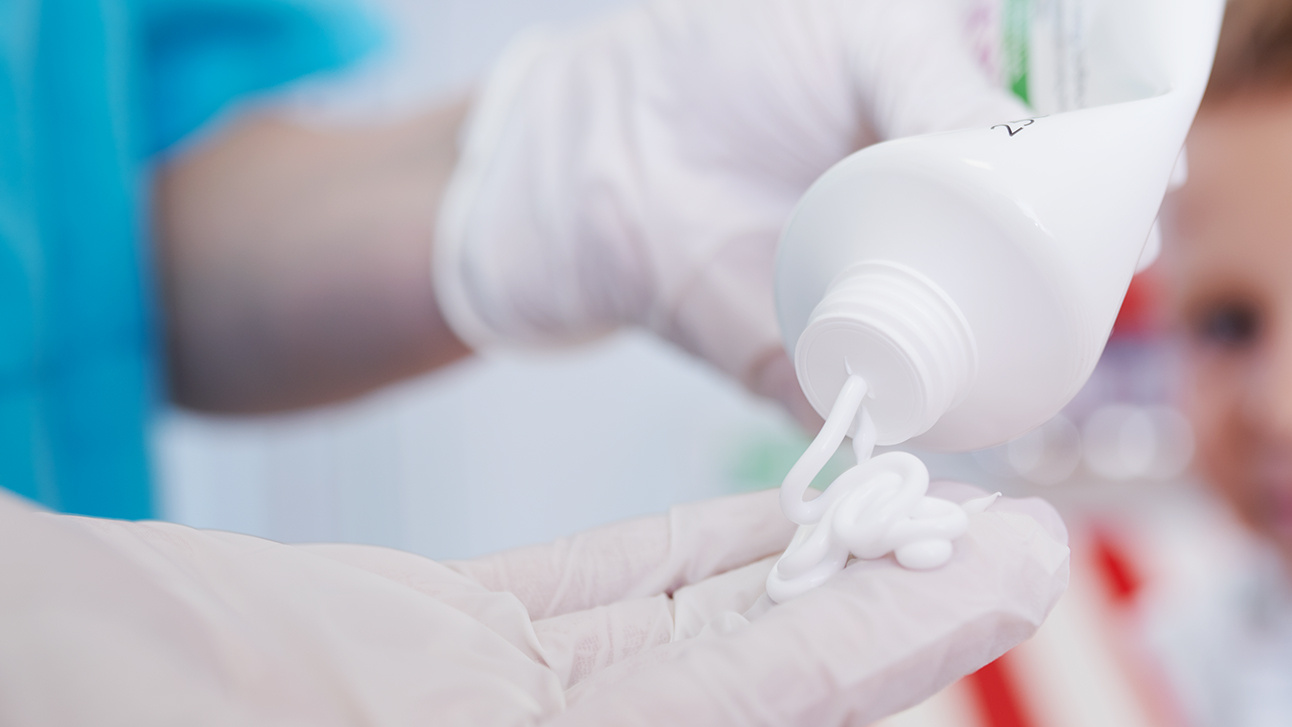 Creme wird aus Tube auf eine Hand ausgedrückt, die Latexhandschuhe trägt.